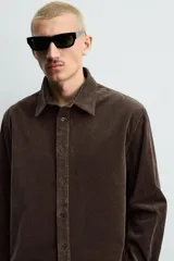 Camisa de corte relajado confeccionada en pana de algodón, con cuello solapa, manga larga con puños abotonados y cierre frontal de botones.