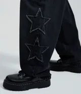 Pantalón de jean color negro con corte baggy y cintura media. Presenta estrellas bordadas con acabado desflecado en las piernas y bolsillos funcionales.