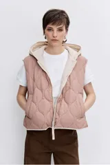Chaleco reversible con capucha, diseño acolchado con costuras onduladas, cierre frontal y bordes en contraste. Presenta un lado en tono rosado y el otro en tono beige.