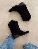 Bota corta de gamuza color marrón topo, estilo western, con bordados decorativos en hilo blanco en caña y empeine. Posee taco cuadrado de madera y punta ligeramente afilada.