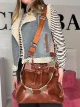 Bolso tipo bucket Chabas modelo Marin, confeccionado en cuero genuino de color marrón. Cuenta con diseño de cordón ajustable fruncido en la parte superior, manija corta decorativa de cuero con detalles metalizados y una correa larga intercambiable.