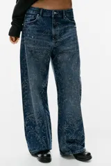 Jeans baggy de tiro medio con cinco bolsillos, trabillas para cinto y cierre frontal con cremallera y botón metálico. Cuenta con detalle de aplicación de brillos en toda la prenda.
