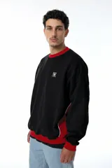 Buzo de corte oversize con diseño colorblock en negro y rojo. Presenta cuello redondo, puños y cintura acanalados, y paneles laterales con vivos blancos. Incluye logo bordado en el pecho.