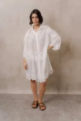 Camisola blanca de silueta amplia y caída liviana, con bordados florales sutiles, cuello camisero, cierre frontal de botones y mangas 3/4.