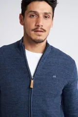 Campera tejida de punto en color verde militar, con cierre frontal completo, cuello elevado y ajuste regular. Presenta un diseño texturizado con logo bordado en el pecho y puños acanalados.