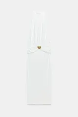 Vestido midi blanco de cuello halter, confeccionado con mezcla de poliamida. Presenta detalle de drapeado lateral con un broche metálico dorado en forma de caracola y cierre en la espalda ajustable con lazadas.