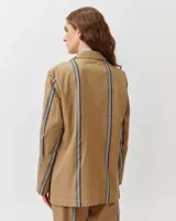 Blazer de algodón color tostado con cierre de un botón, solapas clásicas y bolsillos con solapa. Presenta detalles de bandas rayadas verticales a lo largo del frente, mangas y espalda.