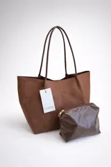 Bolso tipo shopper de material sintético con acabado efecto gamuza en color marrón, con asas largas para llevar al hombro. Incluye un neceser interno de material brillante a tono con cierre metálico.