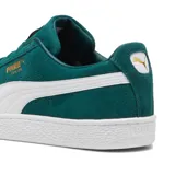 Championes Puma modelo Suede Classic, confeccionados en gamuza de color negro con la icónica franja lateral en blanco y el logotipo de la marca impreso en dorado metalizado en el lateral. Suela de goma texturizada en color blanco.