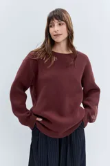 Sweater de punto color bordó, con cuello redondo, manga larga y diseño holgado. Presenta detalles bordados en hilo dorado en la zona del hombro y en el puño.