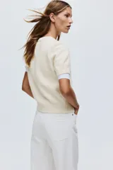 Buzo de punto suave con cuello redondo y mangas cortas. Presenta un ajuste entallado con terminaciones acanaladas en cuello, puños y bajo.