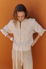 Bomber de tela liviana color beige con textura sutil, cierre frontal completo, mangas largas con puños elásticos y cordón ajustable en el ruedo.