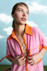 Túnica de algodón color negro, con cuello polo, manga corta, cartera frontal con botones y bolsillo ojal en el pecho. Presenta detalles de voladitos mostaza en el cuello, la botonera, los puños, el bolsillo y el ruedo.