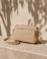 Bandolera color beige con tres compartimentos con cierre, herrajes dorados y correa ajustable.