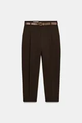 Pantalón tobillero de tiro medio, color beige, con pinzas delanteras y bolsillos frontales. Incluye un cinturón fino de cuero marrón con hebilla metálica dorada y cierre frontal con cremallera, botón interior y gancho.