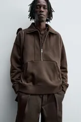 Sudadera de corte relajado color marrón oscuro, con cuello subido y cierre frontal de cremallera. Presenta manga larga, bolsillo frontal tipo canguro y acabados en rib en puños y ruedo.