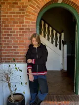 Campera negra con cierre frontal, capucha y puños con rayas rojas y blancas.