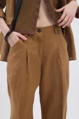 Pantalón de lino marrón de tiro medio, con calce holgado y diseño de piernas amplias. Cuenta con bolsillos traseros, trabillas para cinto y un pin bordado en contraste.