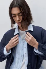 Campera azul marino de algodón, de corte relajado y largo corto, con cuello redondo, cierre frontal con botones metálicos, bolsillos delanteros y mangas largas con puños ajustables.