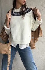 Sweater de punto color natural con cuello redondo y detalle de guarda tejida en la parte superior del pecho. Presenta mangas largas con puños acanalados y un diseño de corte recto.