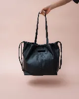 Cartera tipo tote de cuero negro con diseño fruncido en la parte superior y cierre mediante cordones laterales. Cuenta con asas largas para llevar al hombro y un asa superior integrada para llevar en la mano.