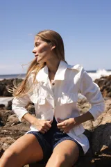 Chaqueta de denim liviana color blanco con volados en el frente, cuello camisero y cierre frontal de botones. Presenta un calce relajado y bolsillos funcionales.