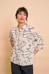 Camisa blanca de manga tres cuartos con diseño estampado de hojas en color azul oscuro, cuello camisero y cierre frontal con botones.
