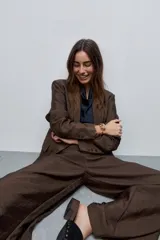 Blazer de silueta amplia y largo por debajo de la cadera, confeccionado en tela liviana con brillo sutil y caída fluida color marrón. Presenta cuello con solapas, cierre frontal, bolsillos con tapa, mangas largas y abertura posterior.