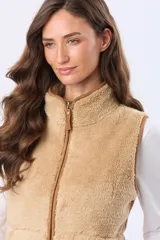 Chaleco de tejido sherpa color beige, con cuello alto y detalles en eco cuero. Diseño sin mangas que proporciona abrigo al torso manteniendo la libertad de movimiento.