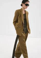 Blazer de lino color verde militar, de corte recto y diseño estructurado, con cuello en pico y solapas de muesca. Presenta mangas largas con puños abotonados, bolsillos con solapa en la parte delantera y cierre frontal de botonadura doble con abertura posterior en el bajo.