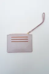 Tarjetero tipo llavero con correa de mano, color lila metalizado, con cierre de cremallera superior y tres ranuras frontales visibles con fondo marrón.