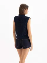 Chaleco color beige confeccionado en tejido semiliviano de galga 12, con calce regular, largo hasta la cadera y escote redondo clásico. Su diseño presenta una trama texturada con figuras geométricas.