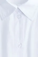 Camisa de algodón blanca, de manga larga con puños abotonados, cuello camisero y cierre frontal de botones. Presenta un diseño con tiras incorporadas en el lateral para anudar, creando un efecto cruzado y drapeado en el frente.