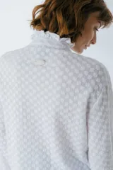 Camisa blanca con textura, cuello alto con volados y cierre frontal con botones.