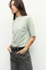 Remera negra de cuello redondo y manga tres cuartos, confeccionada en tela con textura sutil. Presenta fruncidos laterales que aportan caída y movimiento a la prenda.