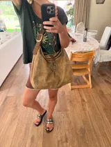 Cartera tipo hobo o de hombro de cuero color camel con efecto gastado. Presenta costuras decorativas en contraste color celeste y un anillo metálico dorado en el frente. Incluye correa ajustable de cuero marrón oscuro con hebilla dorada.