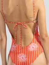 Traje de baño enterizo de lycra color naranja con rayas verticales blancas y estampado de flores rosas. Tiene escote en V, breteles finos y charms florales en los tirantes.