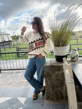 Sweater de punto color crema con diseño geométrico en tonos marrones, naranjas, verdes y grises en el pecho y las mangas. Confeccionado con lana y cuero, con detalles tejidos y bordados a mano.