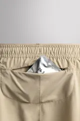 Short deportivo de entrenamiento en color marrón, confeccionado en tejido técnico ligero y elástico. Cuenta con cintura elástica ajustable con cordón, bolsillos frontales, bolsillo trasero con cierre y aberturas laterales en el bajo. Incluye un pequeño detalle de logo estampado en la pierna.