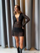 Vestido corto de encaje negro con mangas largas y diseño ajustado. Presenta un escote profundo con detalle de cordones cruzados en el frente.