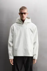 Cazadora deportiva de ajuste regular, confeccionada en tejido técnico de tres capas con membrana impermeable (resistencia al agua ≥15K) y costuras termoselladas. Presenta cuello subido con capucha ajustable, manga larga con puños ajustables con tira adherente, aberturas con cremallera termosellada en axilas para ventilación, bolsillos frontales con cremallera termofijada y bajo ajustable con elásticos laterales.