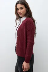 Cardigan de punto con textura de tejido estructurado, color bordó, con cuello redondo, cierre frontal de botones y mangas largas.