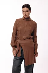 Polera de tejido de punto color marrón, con cuello alto y diseño de trenzas verticales. Presenta mangas largas con puños ajustados y un detalle de panel lateral asimétrico que se anuda en la cintura.