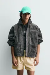 Cazadora de corte relajado confeccionada en piel con acabado de serraje. Presenta cuello solapa, cierre frontal con cremallera oculta bajo solapa con botones a presión, bolsillo con cremallera en el pecho y bolsillos de plastrón con solapa en la cadera. Incluye efecto vintage en las costuras y puños con botón.