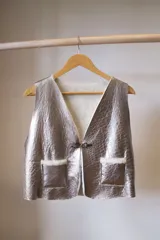 Chaleco reversible confeccionado en cuero genuino. Presenta un lado de piel de oveja gris con bolsillos de cuero negro y un lado de cuero liso gris. Diseño sin mangas con cierre frontal.