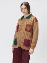 Campera tejida de punto grueso con diseño multicolor. Presenta cuello en contraste de color verde, cuerpo en tono beige con textura trenzada, bolsillos delanteros con apliques en nylon color marrón y bordó, y detalles en nylon en los hombros. Cuenta con cierre frontal de botones y forro interno.