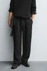 Pantalón negro de corte relajado con cintura elástica ajustable y pliegues en la parte delantera. Presenta bolsillos laterales y bolsillos traseros de parche.
