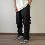 Pantalón cargo parachute negro de corte baggy, con múltiples bolsillos funcionales en los laterales y cordón ajustable con tancas en la botamanga.