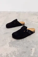 Zueco tipo mule de gamuza negra con hebilla lateral ajustable y suela de corcho con base de goma antideslizante.