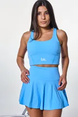 Conjunto deportivo compuesto por un top de escote redondo y una pollera short con diseño acampanado, ambos en color celeste. El top presenta el logo de la marca estampado en el frente.